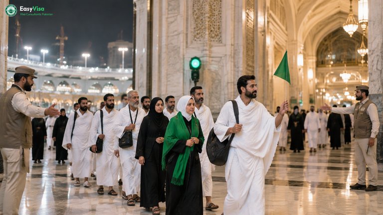 Crowd stewards guiding a Pakistani Umrah group through a gate of Masjid al-Haram with green crowd-signal lights on a Ramadan night